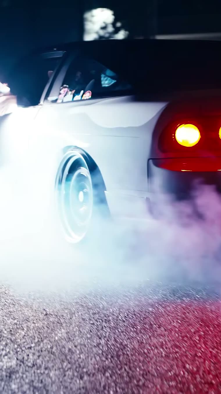 Car mid burnout at night, tail lights glowing through tyre smoke